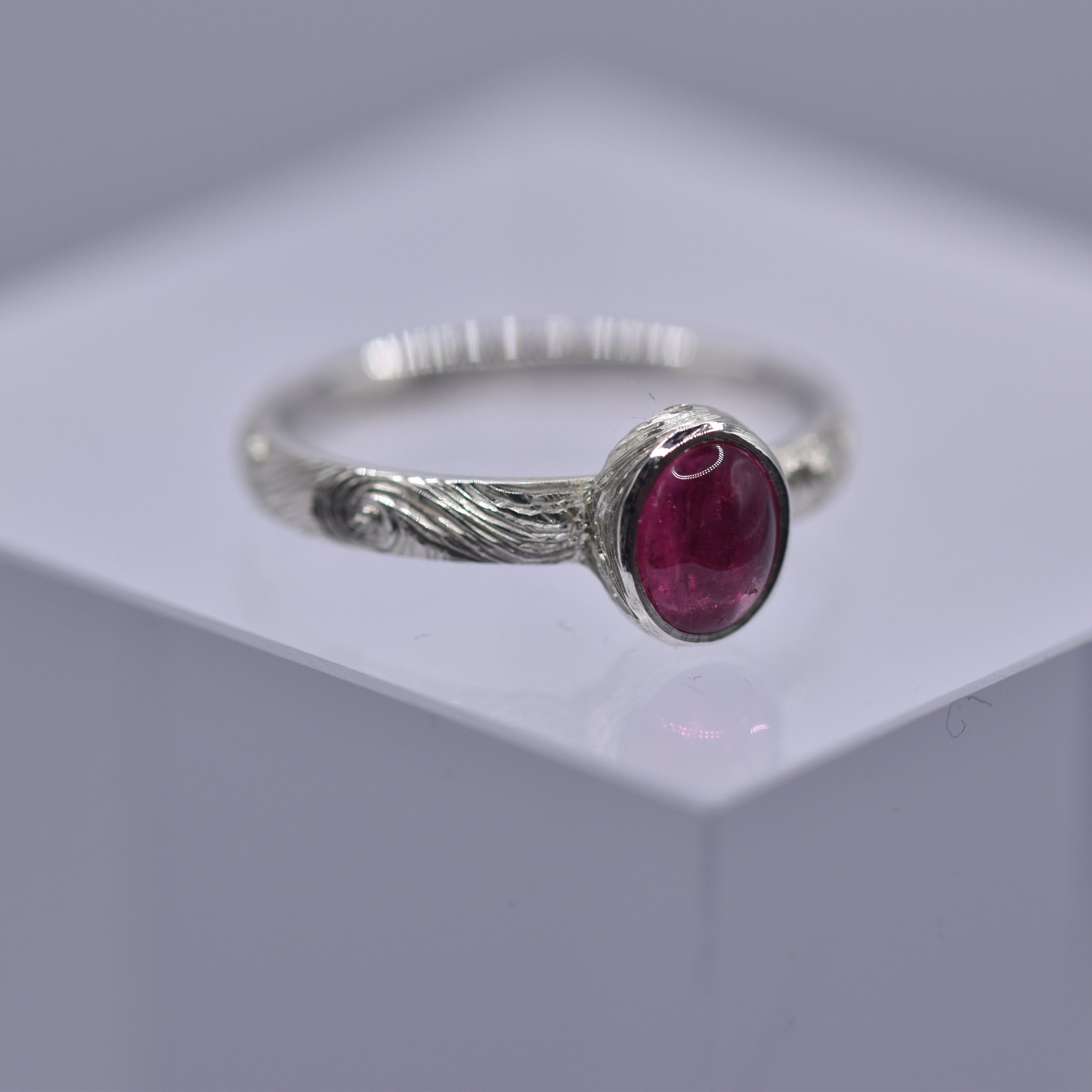 Silver ring with a pink gemstone with swirls and waves engraved on the ring on a gray background