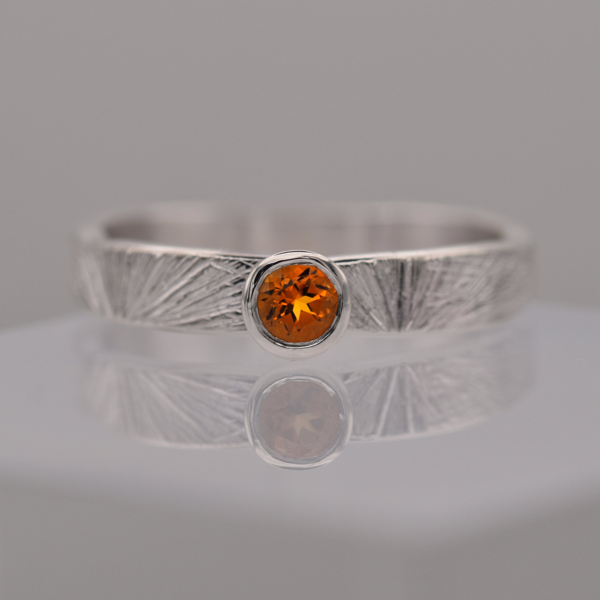 Silver patterned ring with a round orange/yellow citrine gemstone on a gray background