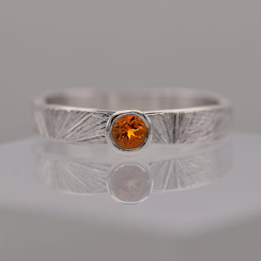 Silver patterned ring with a round orange/yellow citrine gemstone on a gray background
