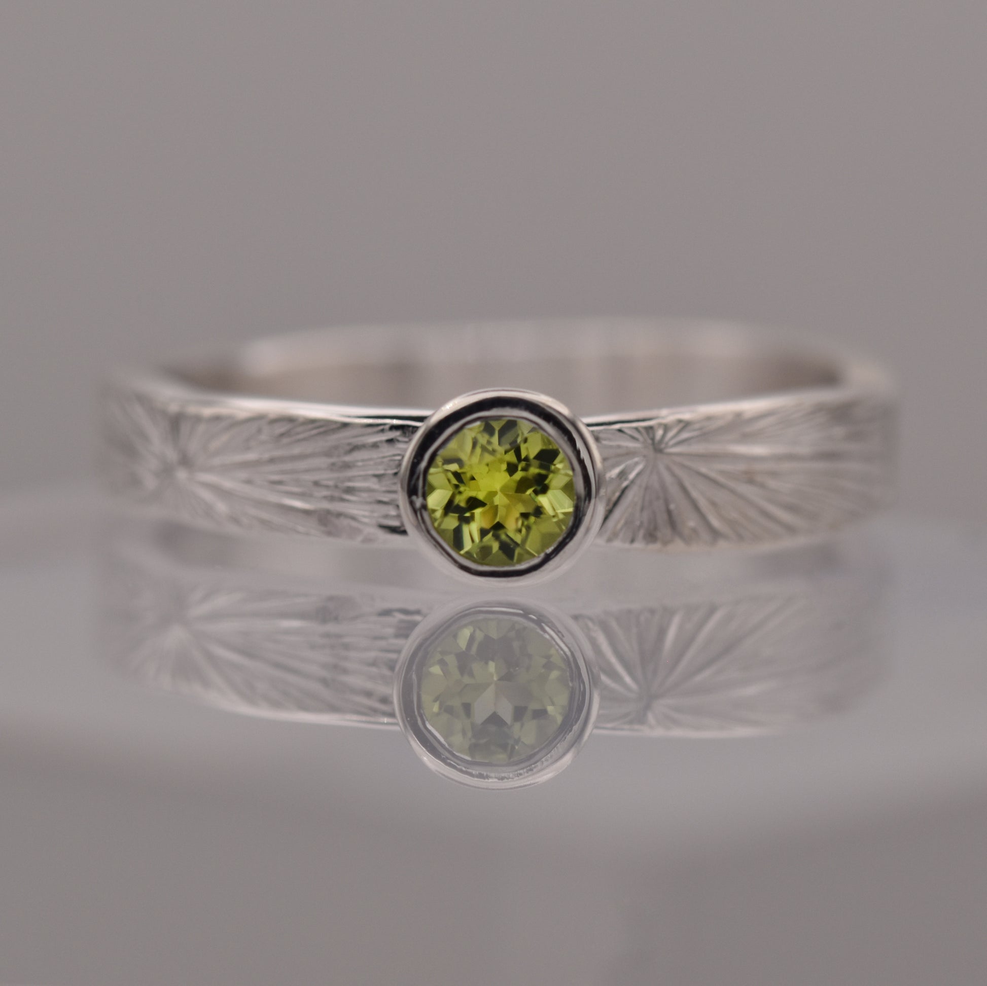 Silver ring with a green gemstone on a reflective surface