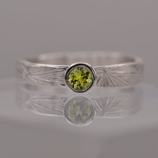 Silver ring with a green gemstone on a reflective surface