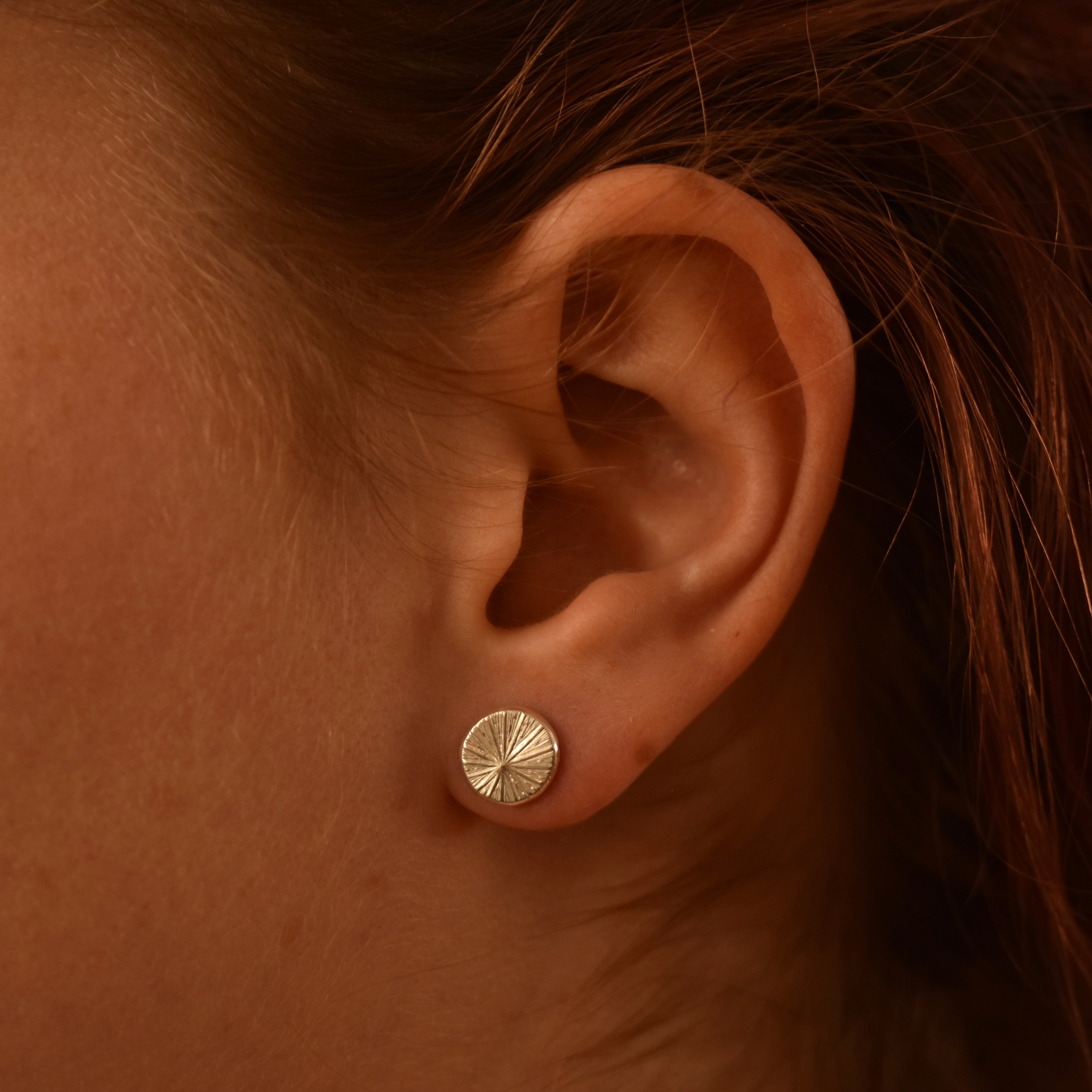 Close-up of an ear wearing a silver earring with a radiating pattern