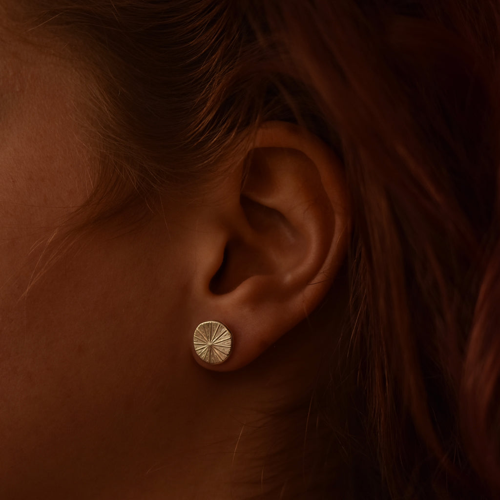 Close-up of an ear wearing a silver stud earring with a radiating design.
