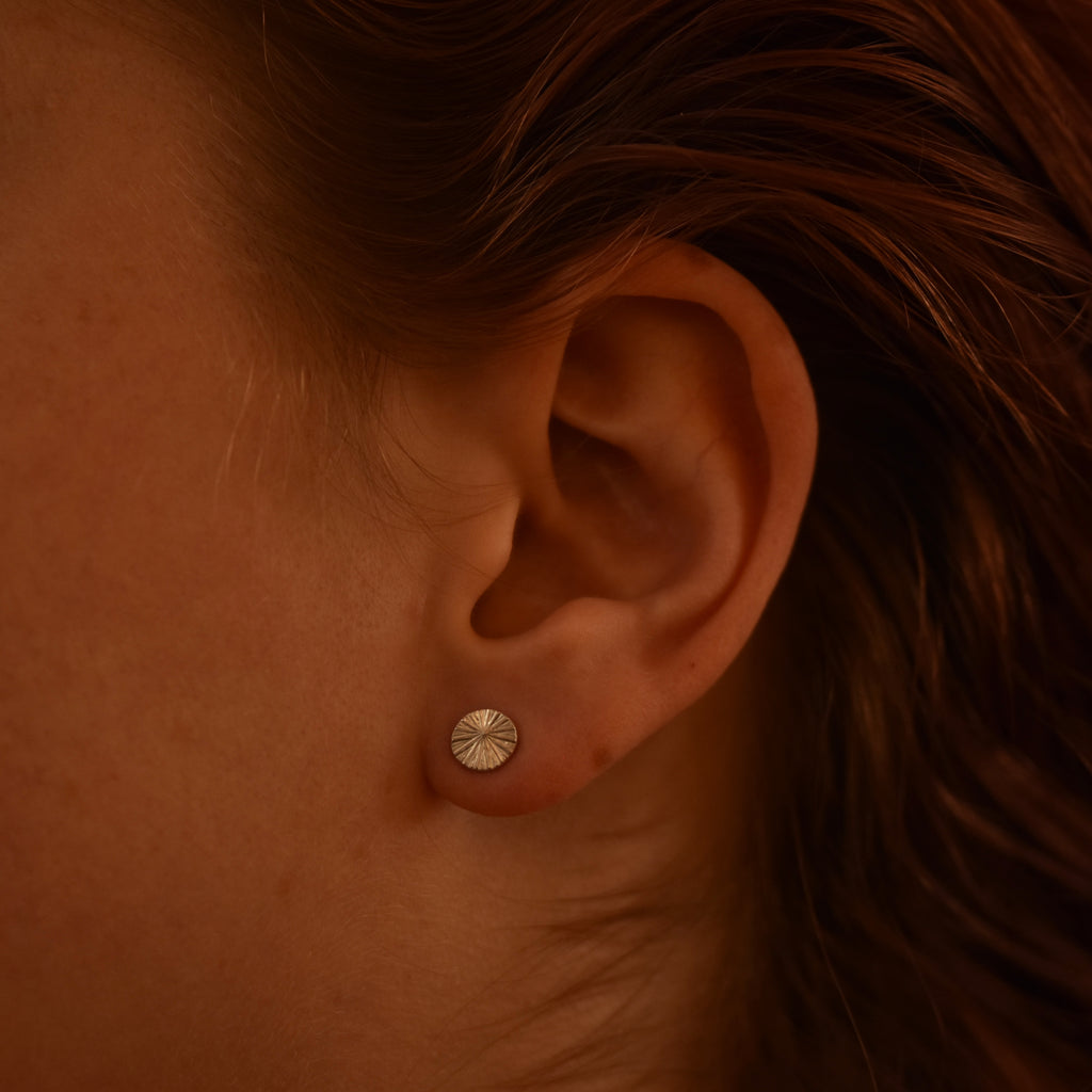 Close-up of an ear with a silver stud earring with radiating pattern