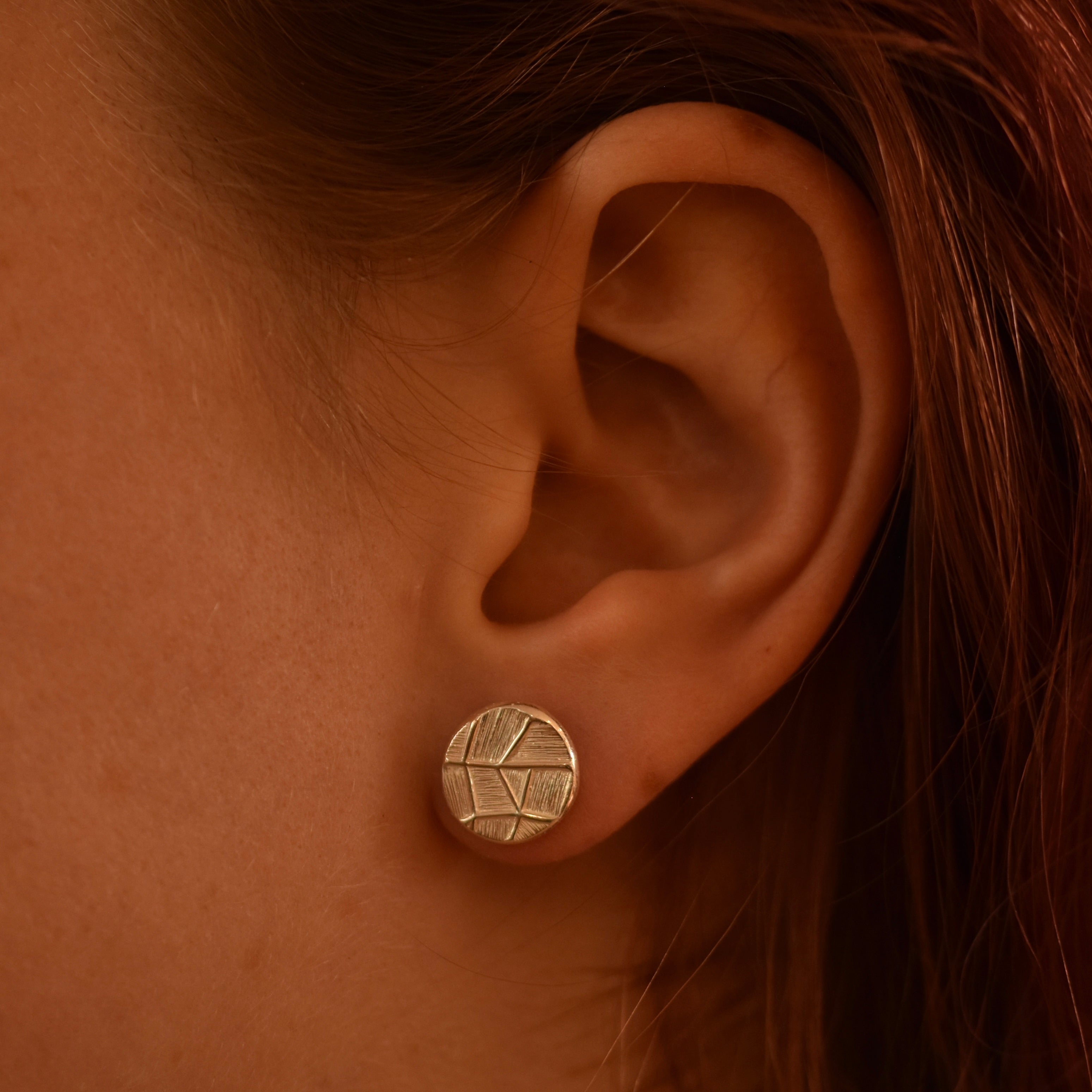 Close-up of an ear wearing a silver earring with a geometric design.