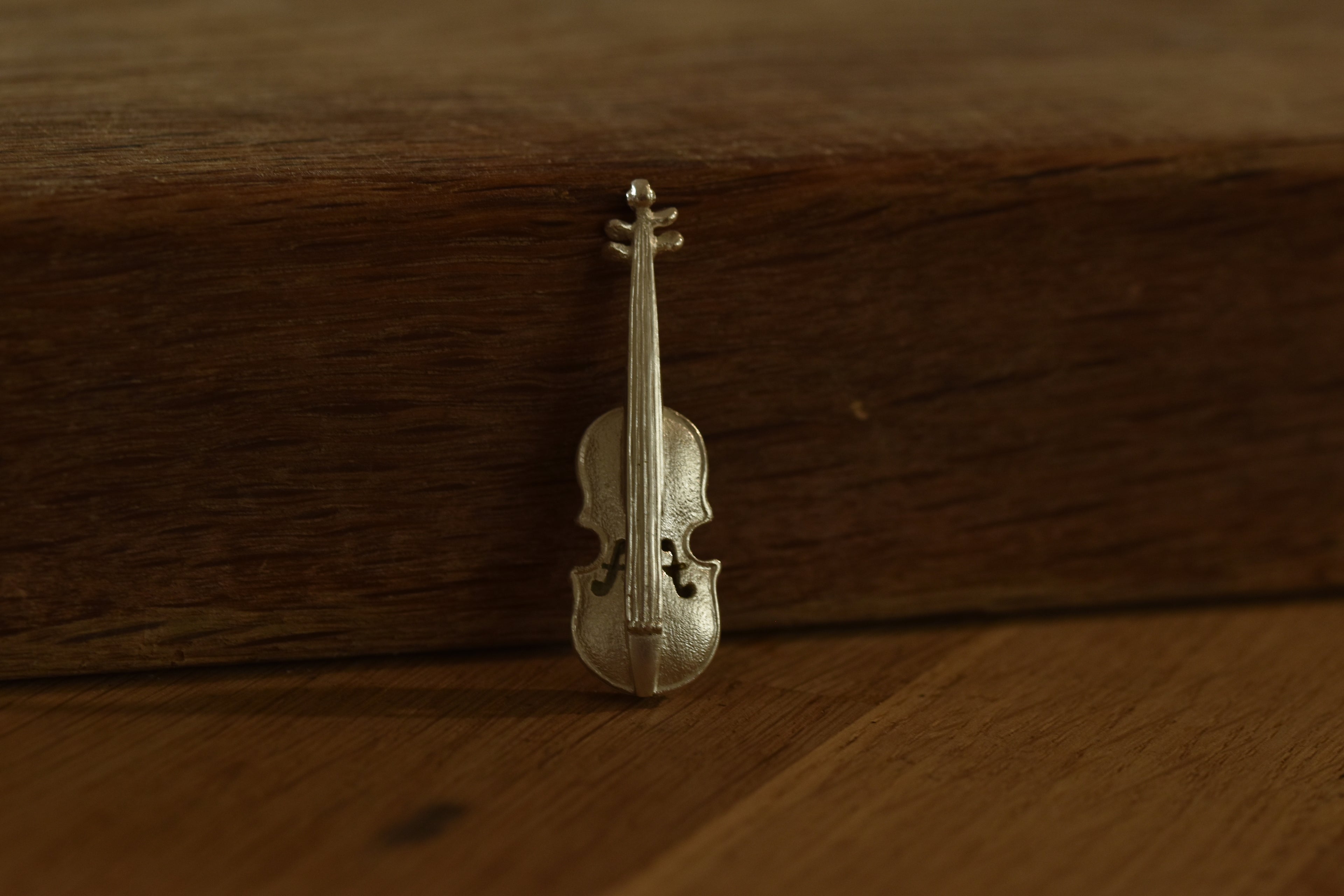 Small silver violin charm on a wooden surface