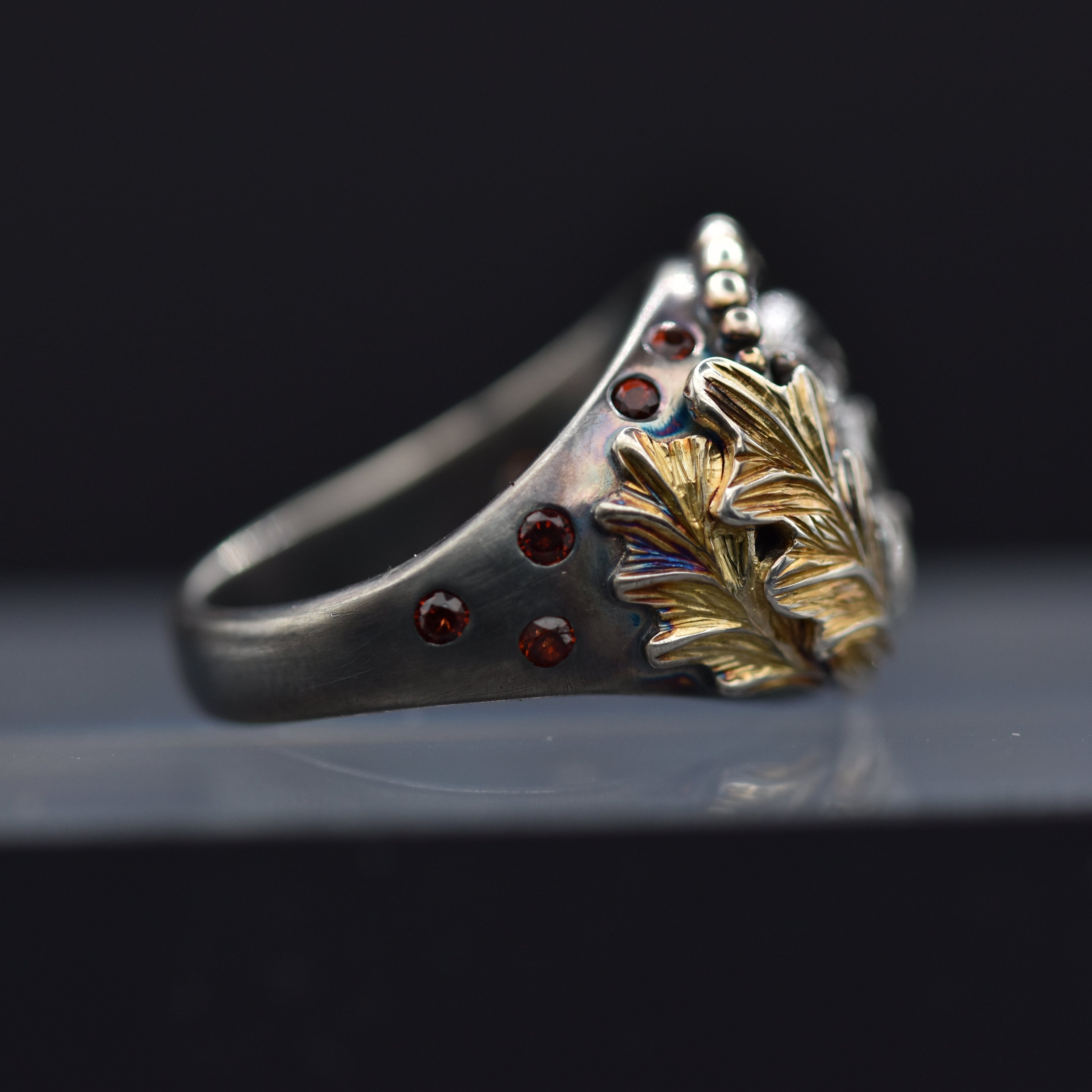 Silver ring with gold leaf and red gemstones on a black background
