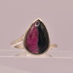 Silver ring with a teardrop-shaped gemstone featuring purple and black colors on a gray background