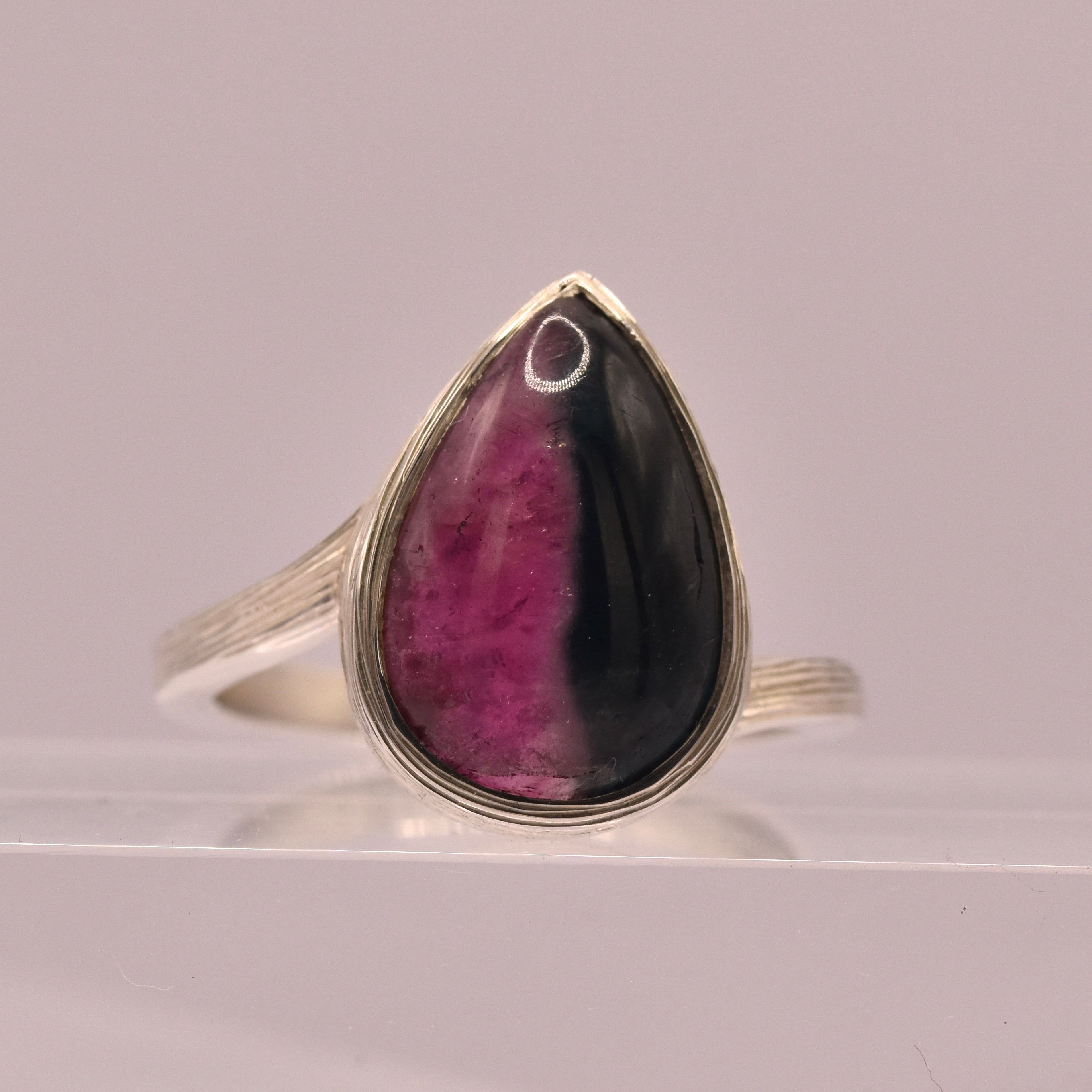 Silver ring with a teardrop-shaped gemstone featuring purple and black colors on a gray background