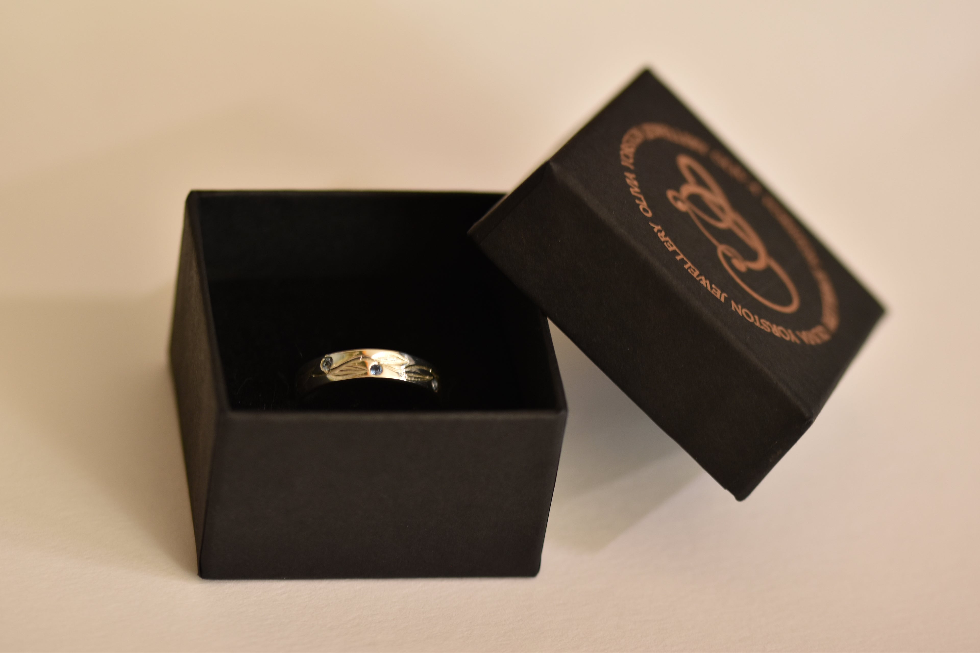 silver ring in a black box with a visible brand logo on a beige background