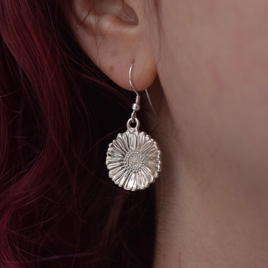 Beautiful sparkly highly detailed and realistic daisy earring on  silver hook. Hanging on an earlobe worn by a girl with red hair. 
