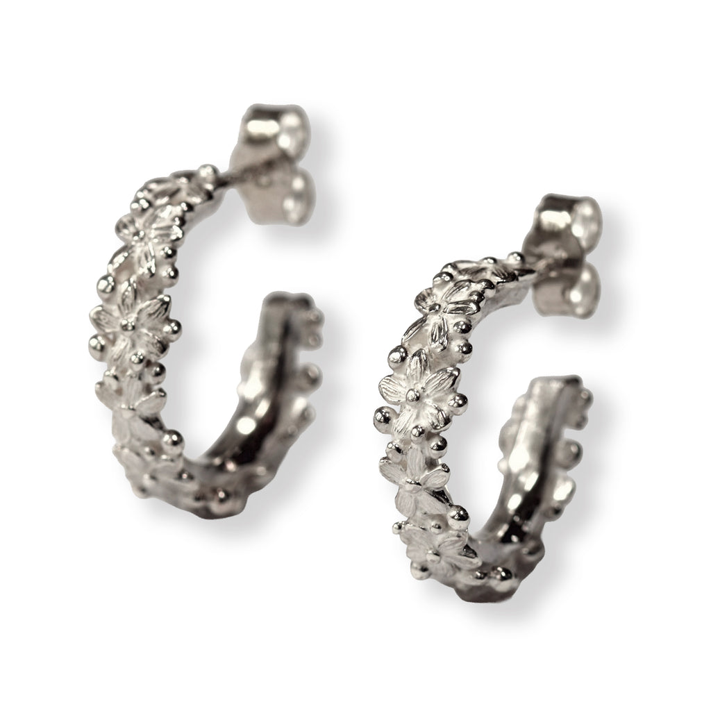 Pair of silver hoop earrings with tiny flowers all the way around on a white background