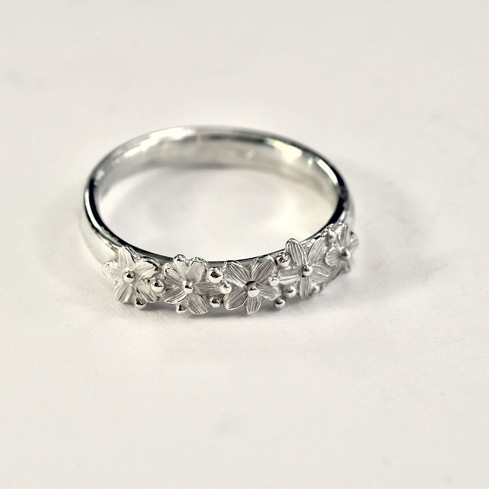 Silver ring with five flowers across the front on a light gray background