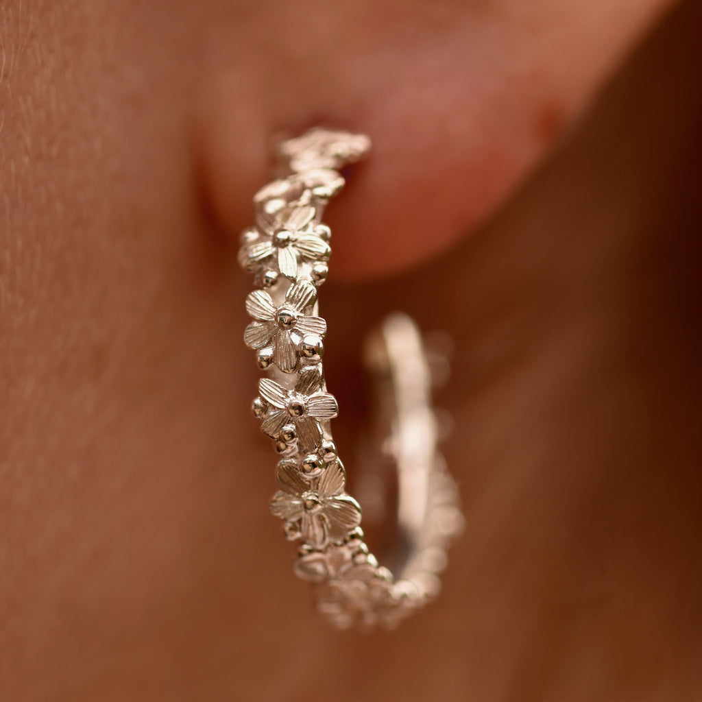Silver floral hoop earrings worn on an ear with a blurred background