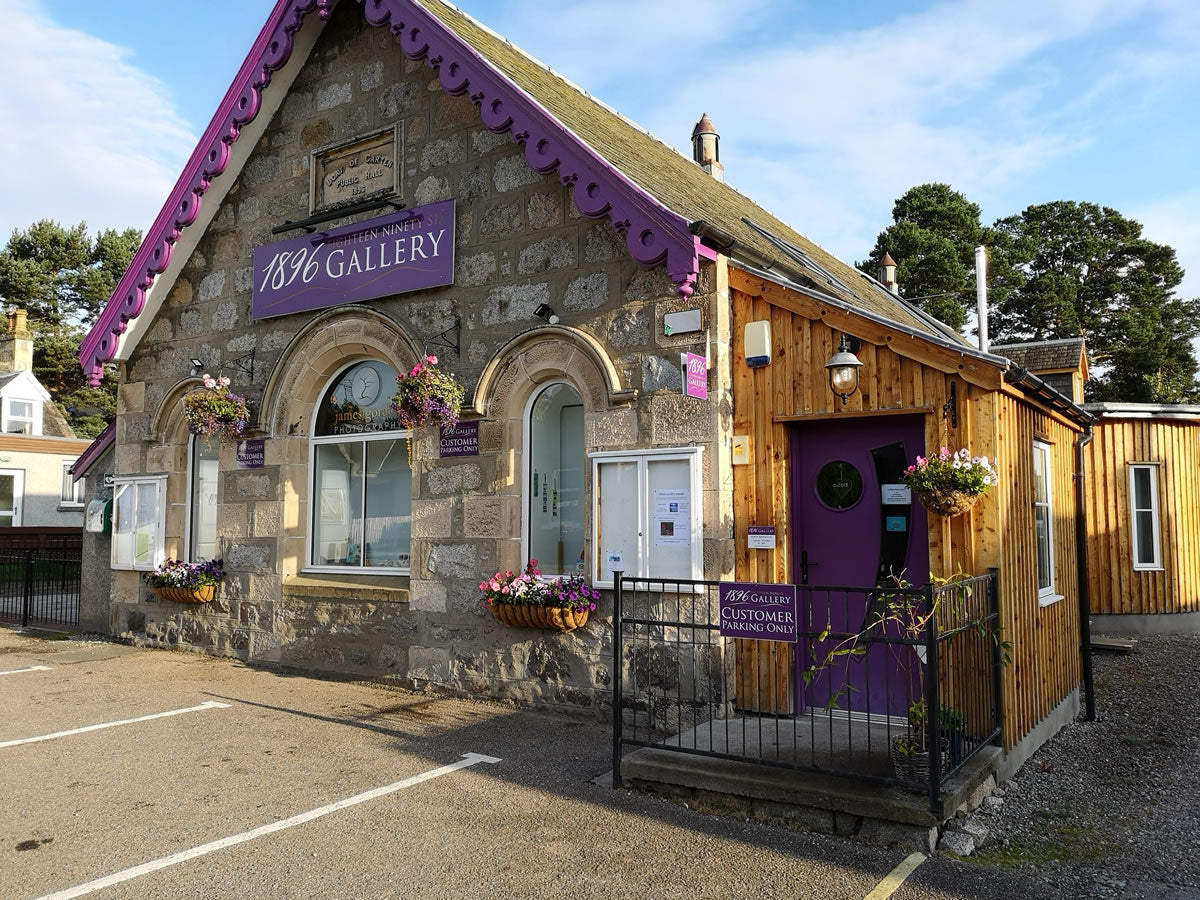 Small building with a purple roof and '1896 Gallery' sign, surrounded by trees and flowers.