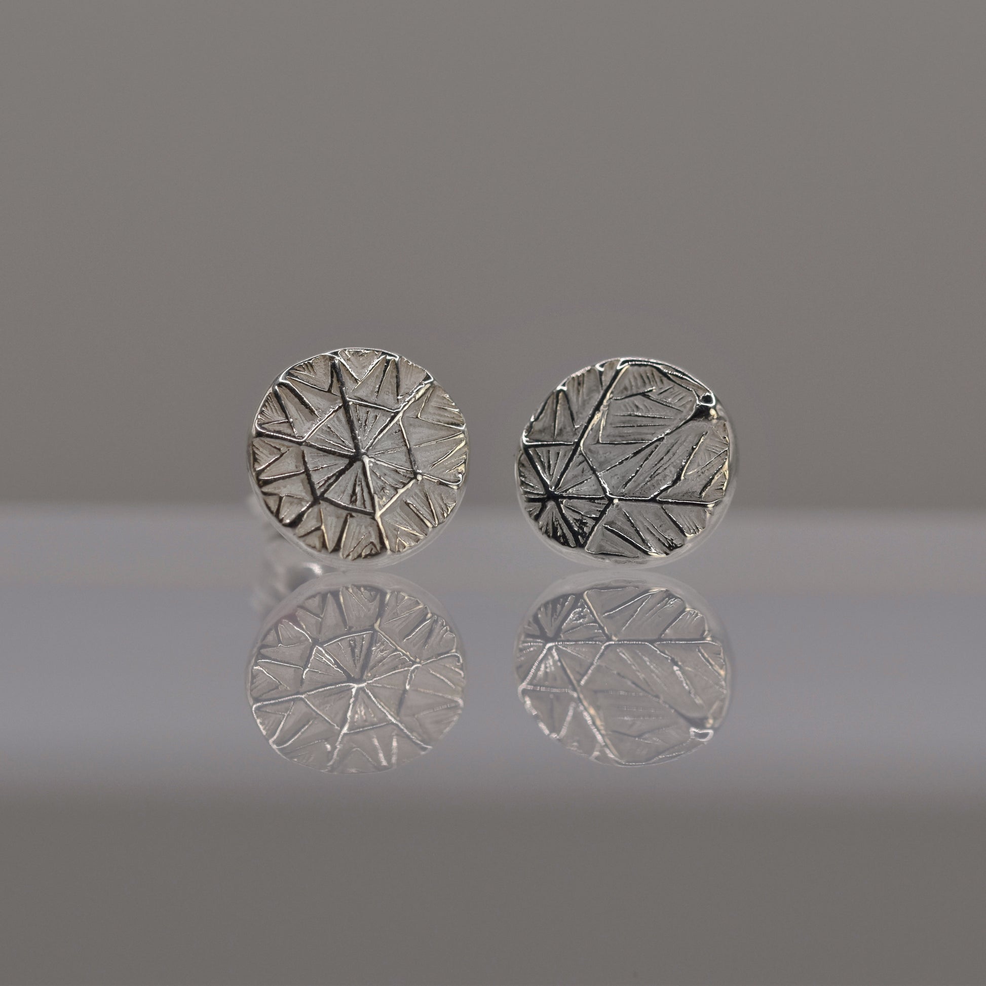 Pair of silver round earrings with textured design of frost pattern on a reflective surface.