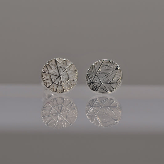 Pair of silver round earrings with textured design of frost pattern on a reflective surface.