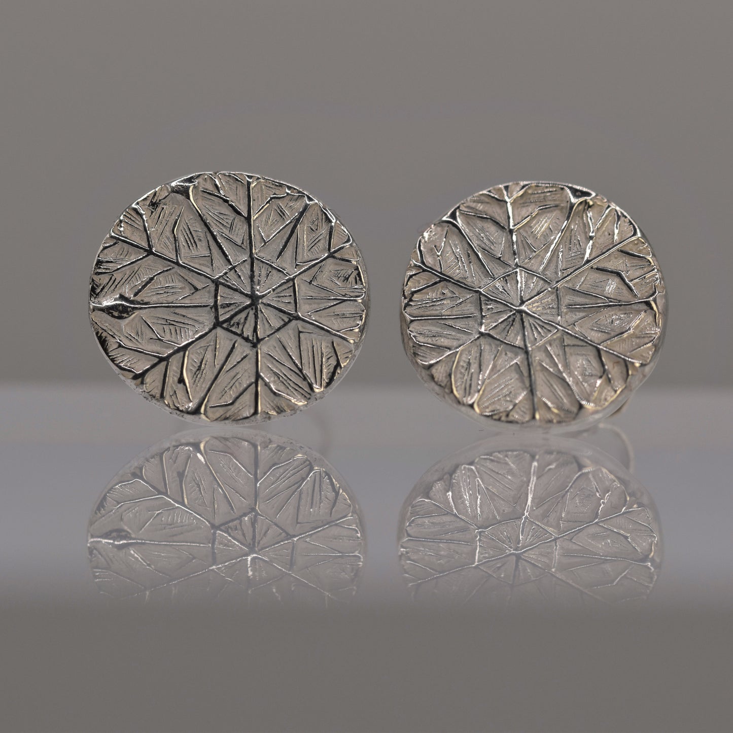 Pair of silver round earrings with textured design of frost pattern on a reflective surface.