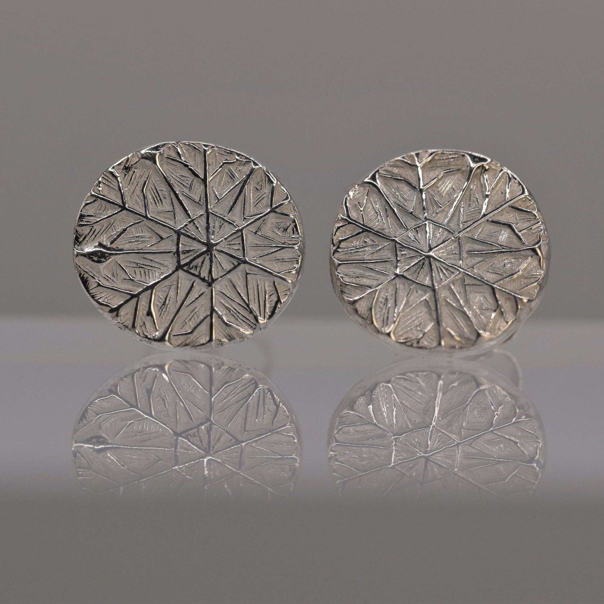 Pair of silver round earrings with textured design of frost pattern on a reflective surface.