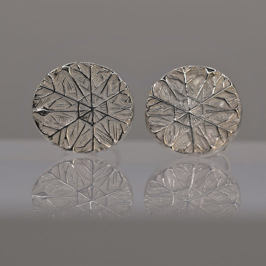 Pair of silver round earrings with textured design of frost pattern on a reflective surface.