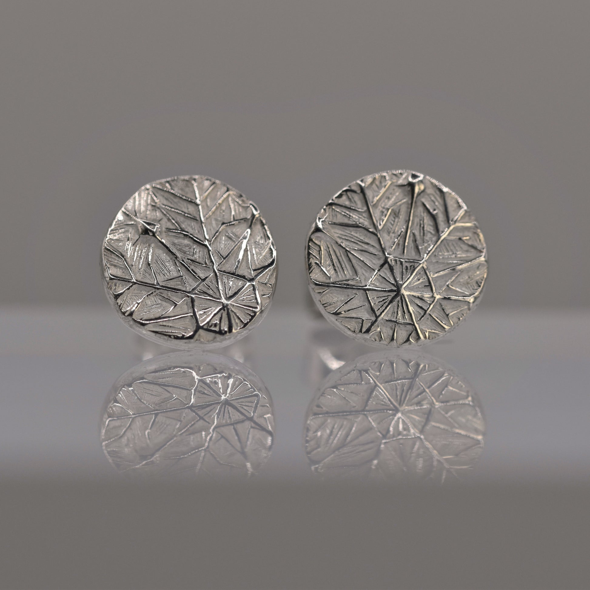Pair of silver round earrings with textured design of frost pattern on a reflective surface.