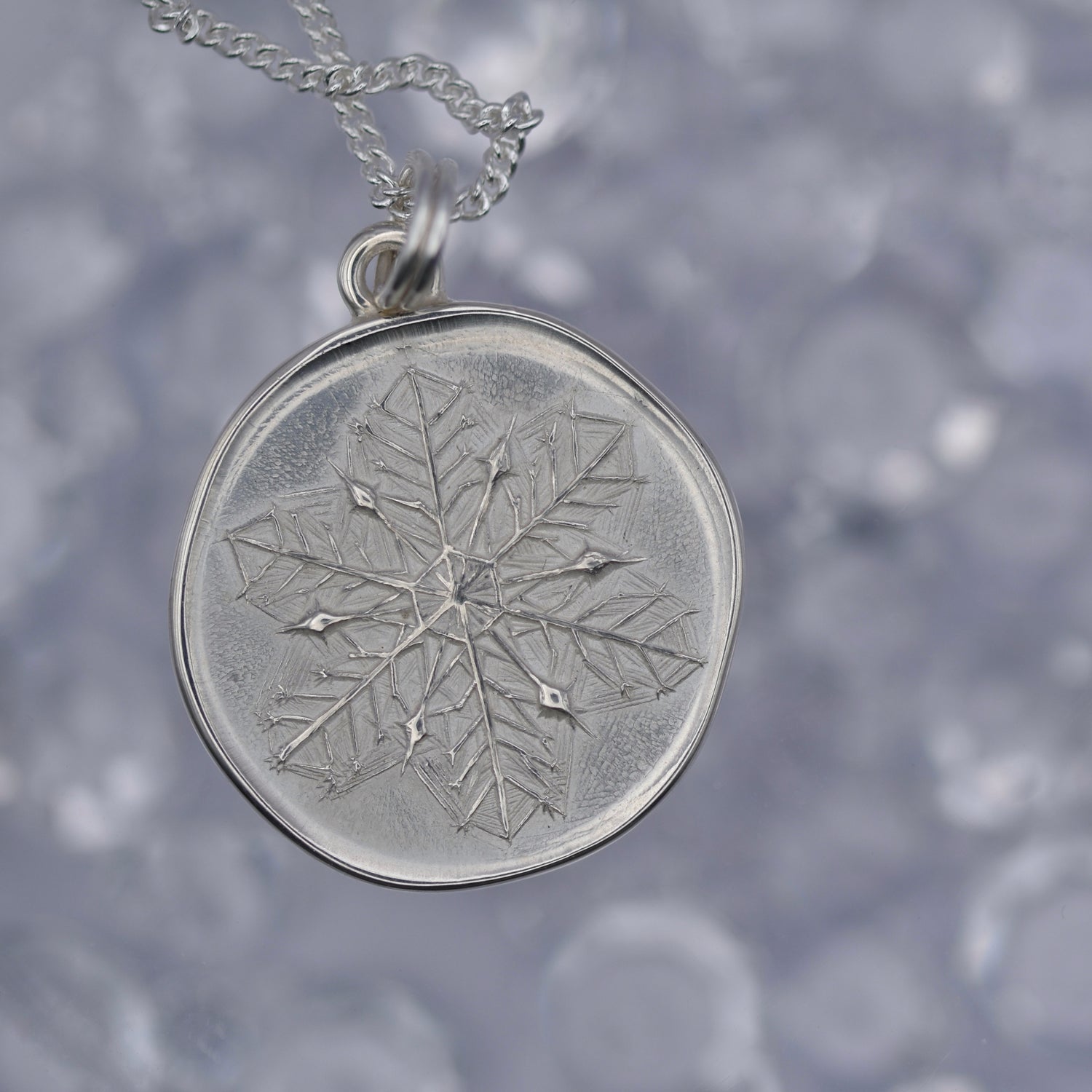 Silver snowflake pendant necklace on a blurred snowy background