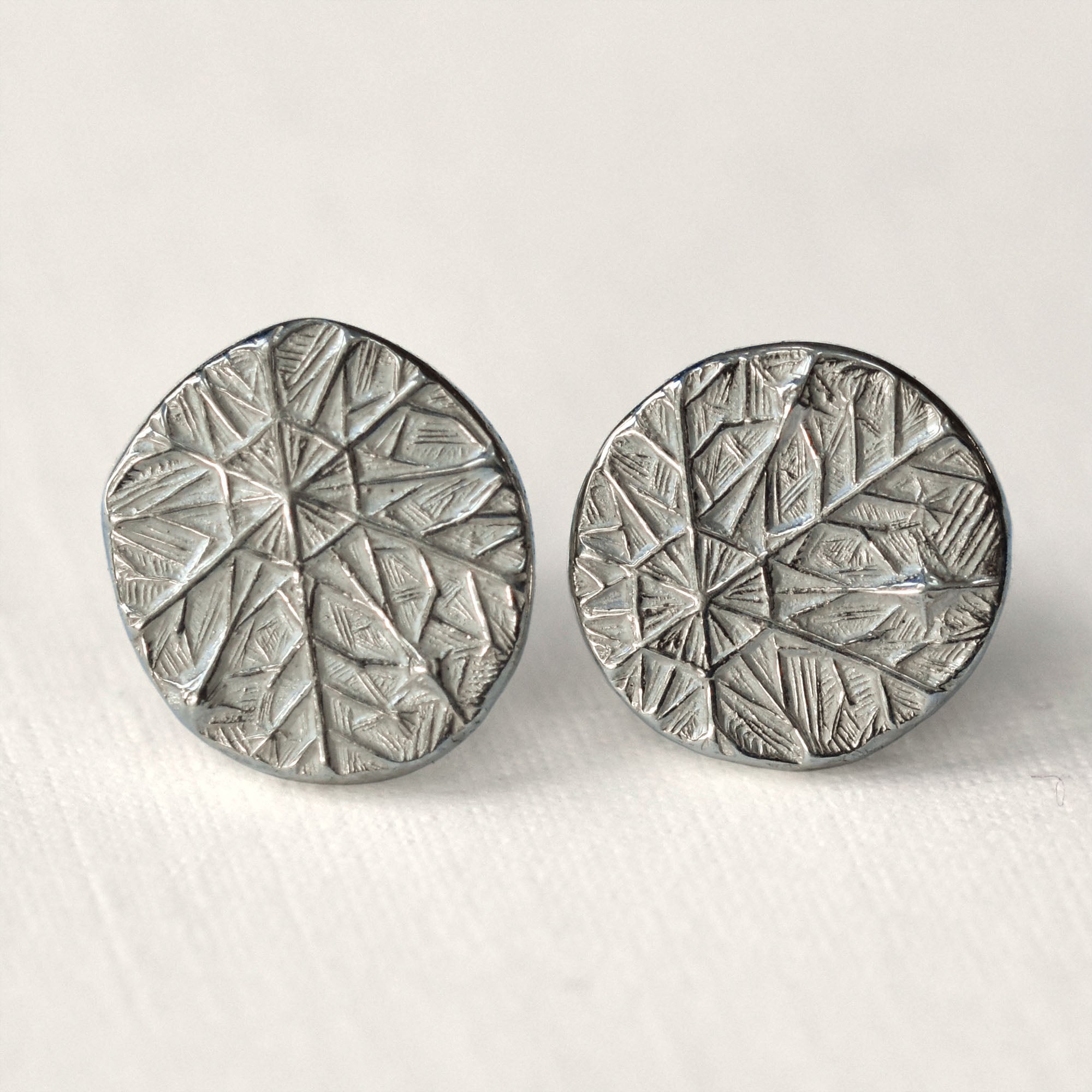 Pair of silver round earrings with frost design on a light gray background