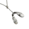 Silver pendant shaped like a sycamore seed on a white background