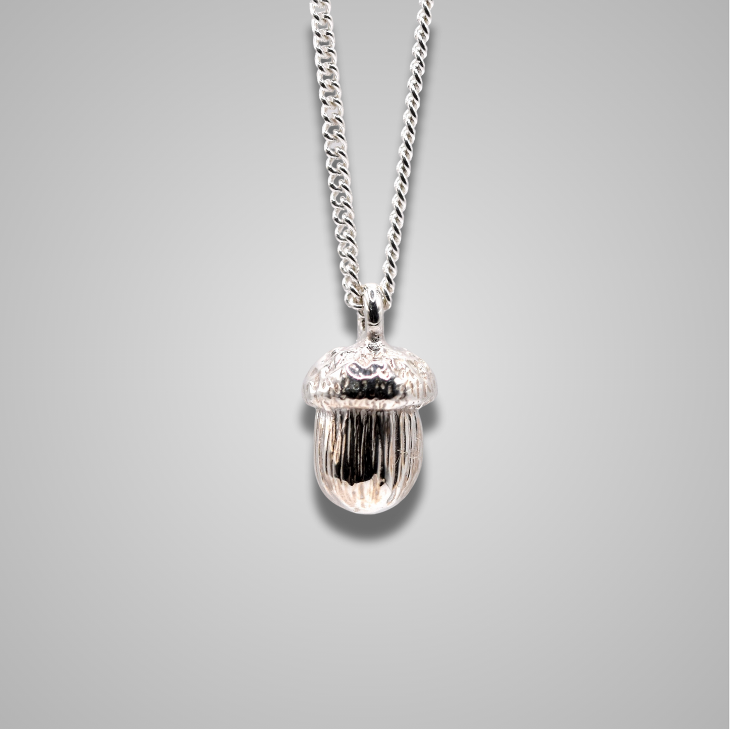Sterling silver acorn pendant hangs from a silver chain. Intricate, realistic and shiny handmade jewellery. 