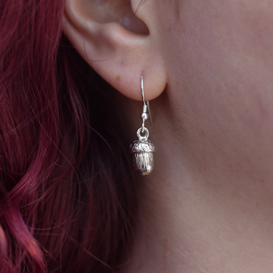 Large drop earring made from silver. The earring is a detailed realistic acorn worn by a girl with red hair 