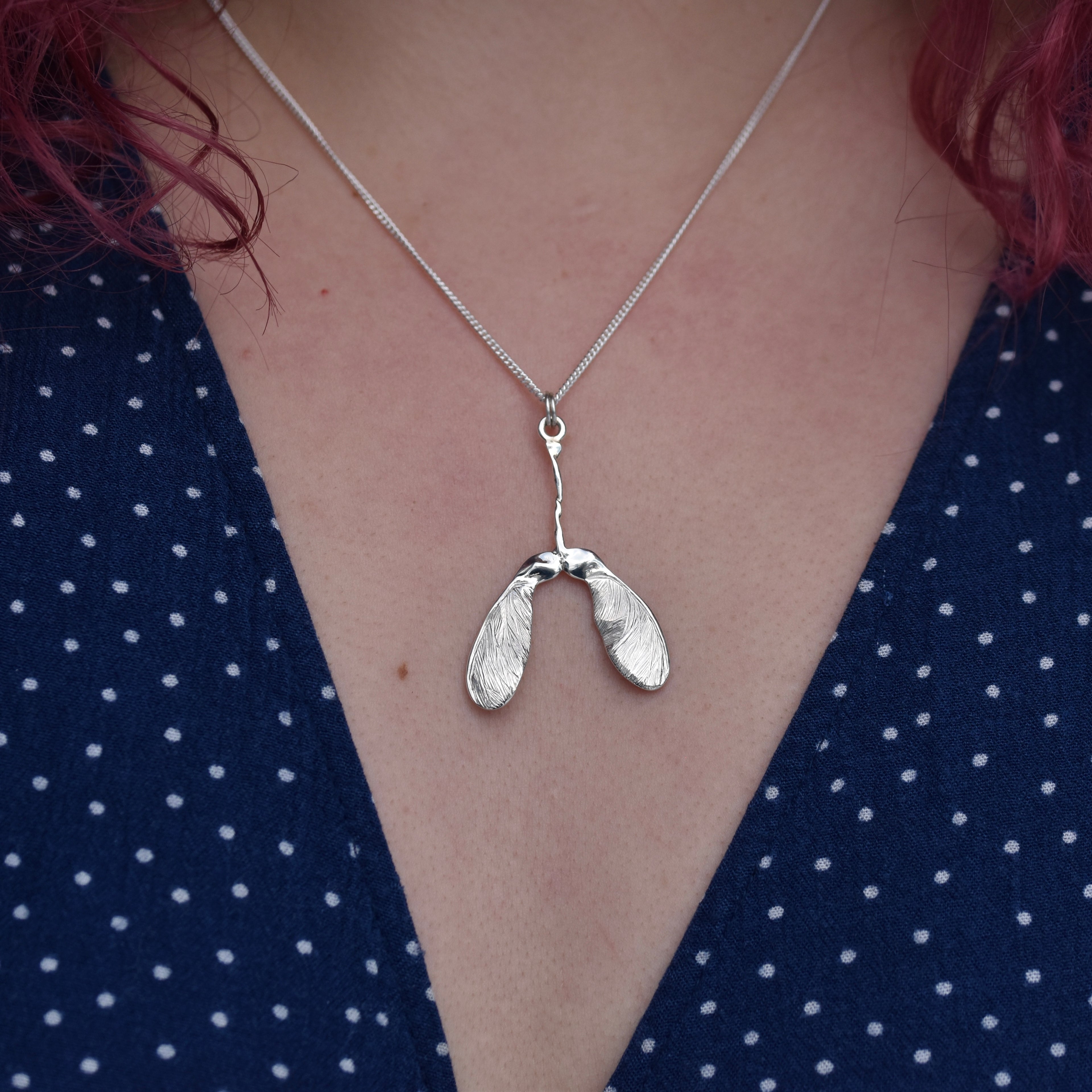 Girl wearing a blue dress is wearing a sycamore seed pendant. The pendant is highly detailed and sparkly with engraved details on a silver chain 