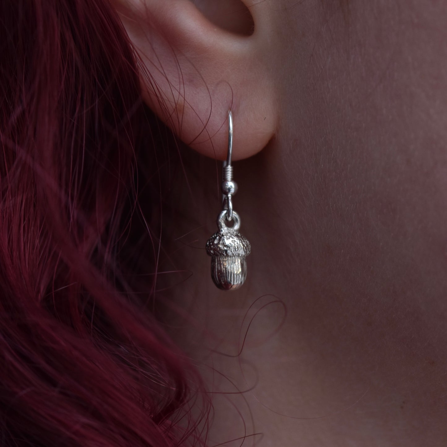 Girl with red hair is wearing a silver earring that is a detailed acorn 