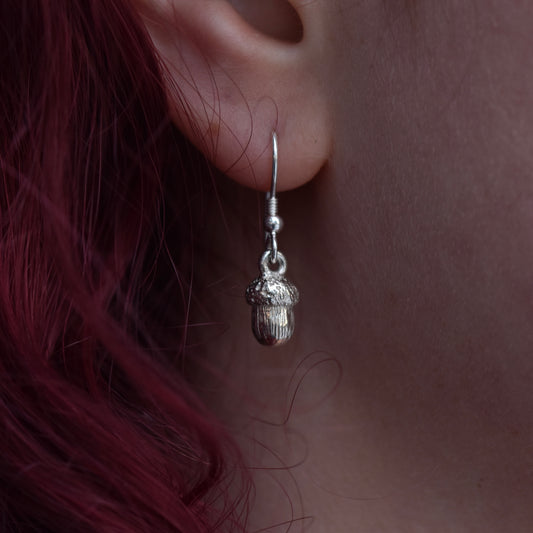 Girl with red hair is wearing a silver earring that is a detailed acorn 