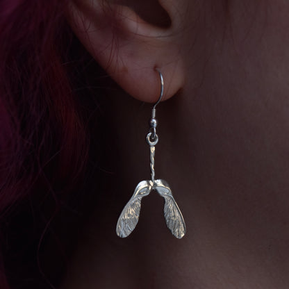 Very shiny earring worn by a girl with red hair. The earring is a sycamore seed covered in sparkley engraving with highly polished silver on a silver hook 