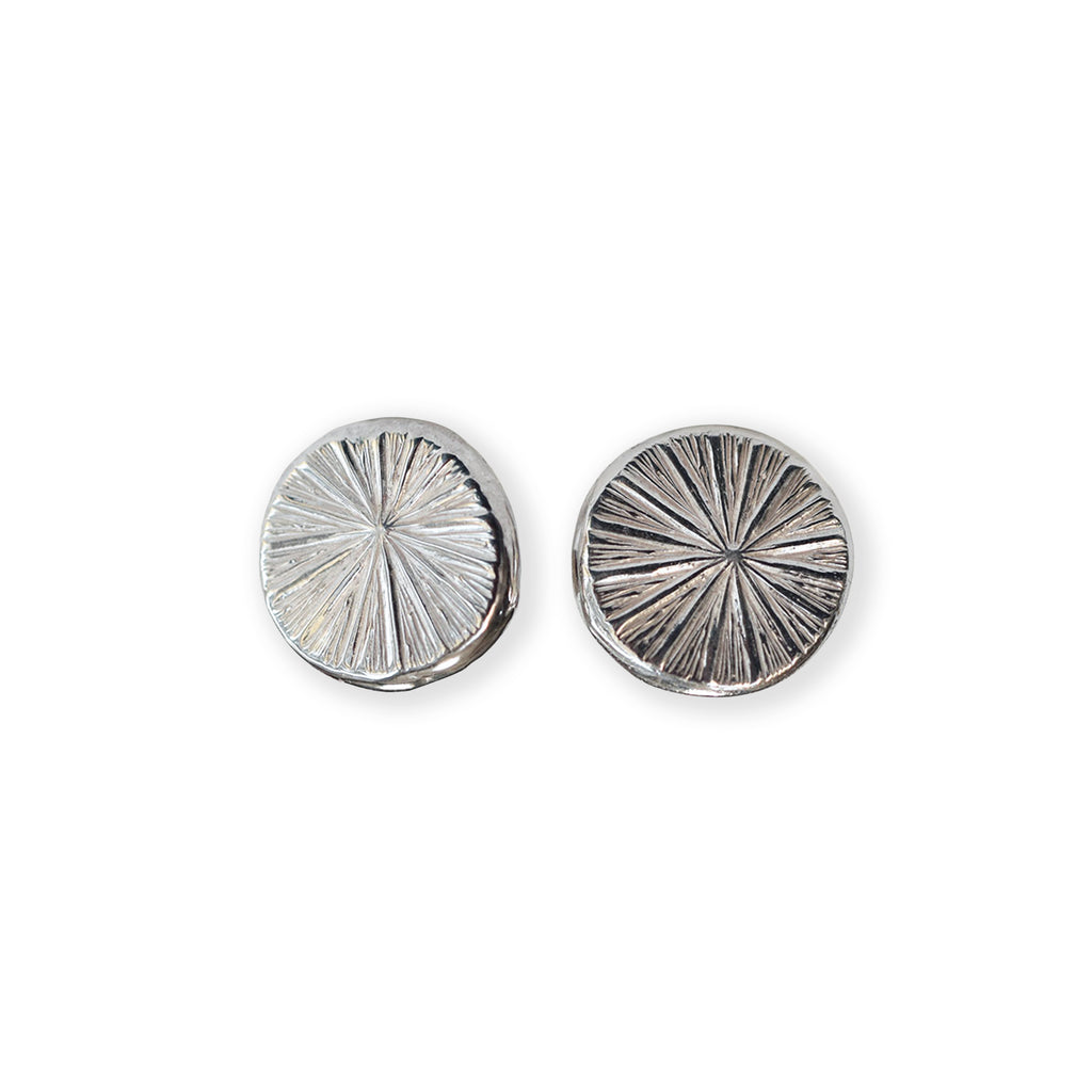 Pair of silver circular earrings with radiating texture on a white background