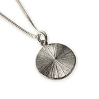 Silver necklace with a textured radiating lines on a  circular pendant on a white background