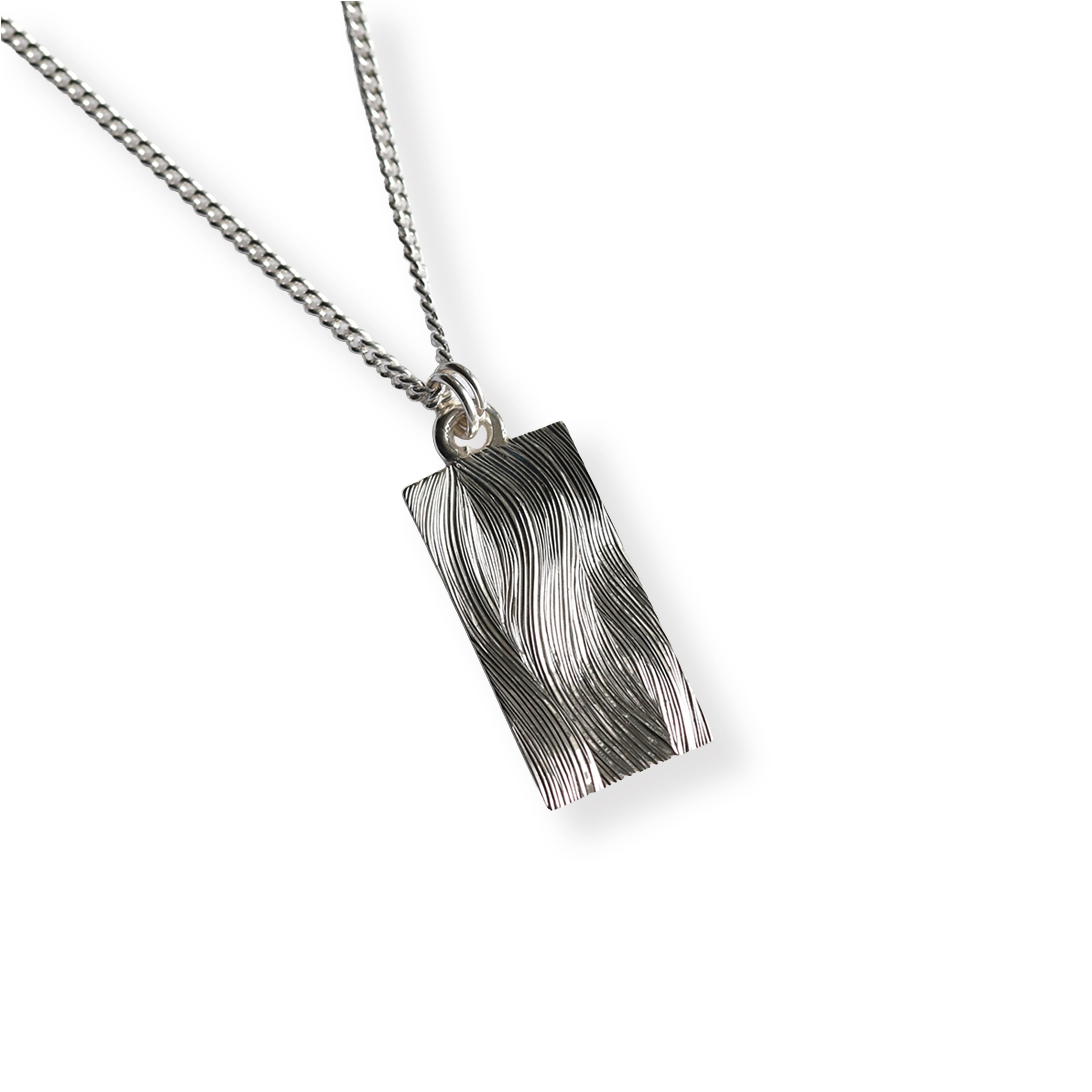 Silver necklace with a textured hand engraved wave patterned pendant on a white background