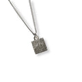 Silver necklace with a textured square pendant on a white background