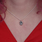 Girl with red hair and v necked top on is wearing a pendant made of silver. The pendant is a tiny curled up squirrel clutching a red gemstone which is a garnet 