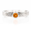 Silver ring with a central orange gemstone on a white background